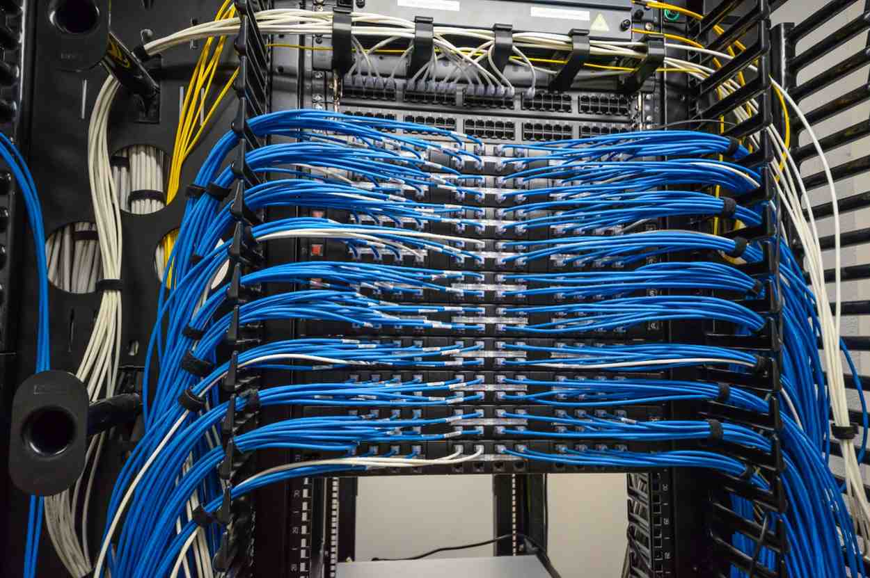 Structured cabling system with bundled blue Ethernet cables connected to network patch panels and switches in a server rack.