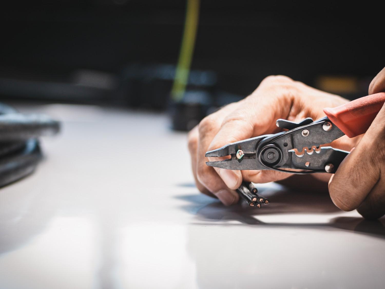 Electrician using a wire crimper and stripper tool to prepare electrical wire for installation or connection.